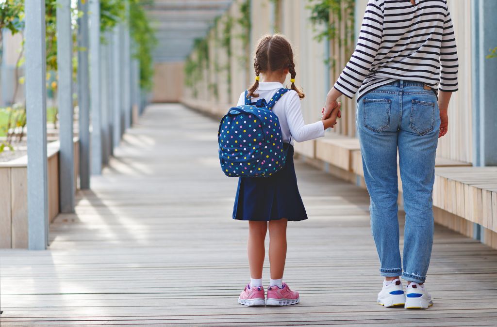A mother holding a child with a back pack - How To Enjoy Summer And Back To School Prep Tips