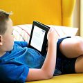 a boy lying on sofa holding tablet Screen Time For Kids During Covid lockdown