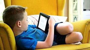 a boy lying on sofa holding tablet Screen Time For Kids During Covid lockdown