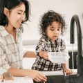 a mother bond with toddler holding a food container at the kitchen sink