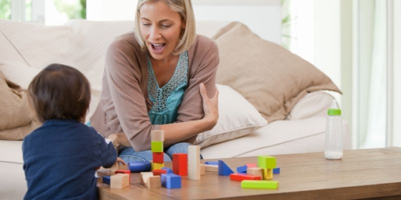 patient parent watches her child playing blocks on top of the table