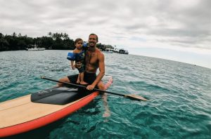 father and kid riding surfboard on the water - father's day getaway ideas