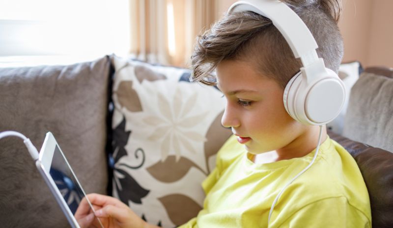A boy wearing white headphones holding a tablet